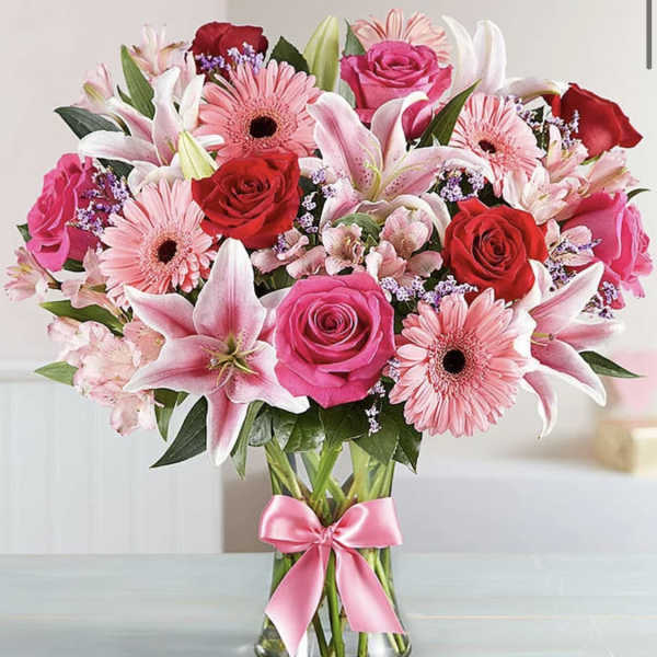 Bouquet of pink and red flowers in a clear glass vase with a pink ribbon