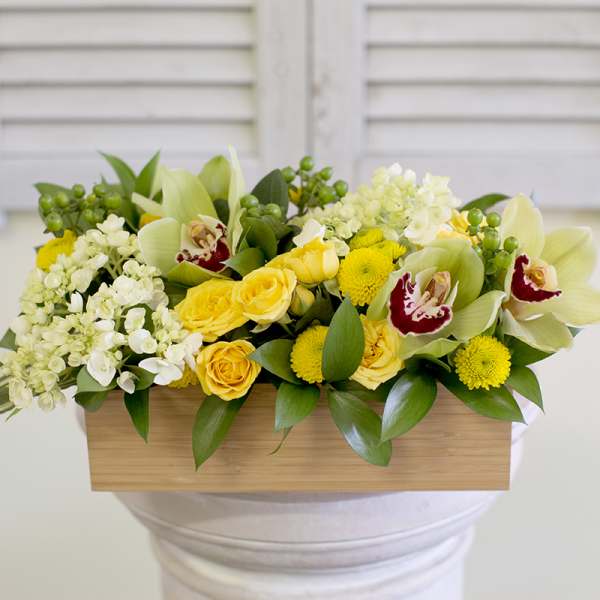 Yellow roses and white orchids in a wooden box arrangement