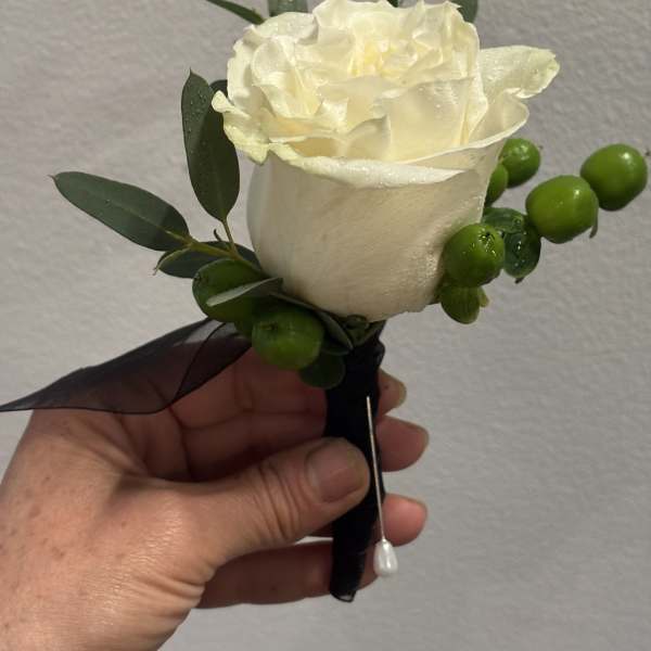 White rose boutonniere with green berries and dark ribbon
