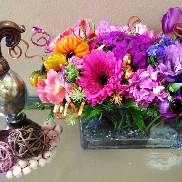 Bright mixed flower arrangement in a rectangular glass vase with decorative curls