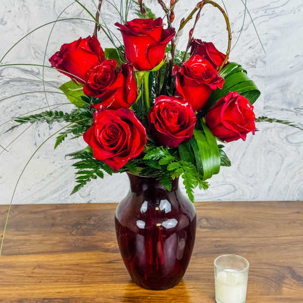 Red roses arranged in a burgundy vase with tall decorative stems