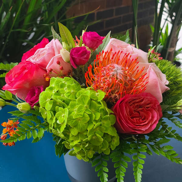 Bouquet of pink roses, green hydrangea, and orange pincushion protea in a vase