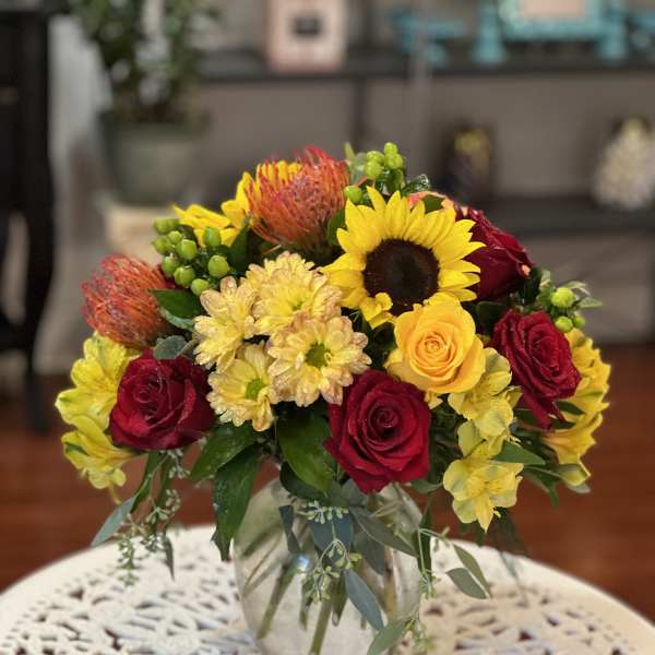 Mixed bouquet of roses, sunflowers, and chrysanthemums in a glass vase
