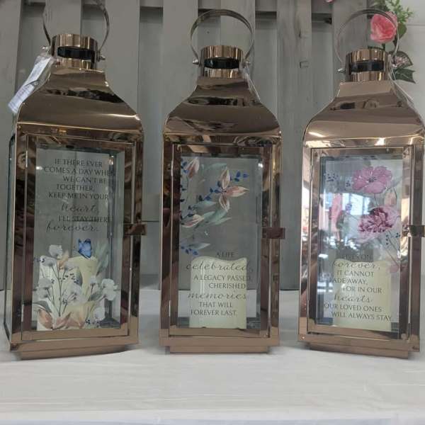 Three rose-gold lanterns with floral inserts and memorial quotes