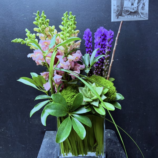 Pink snapdragons and purple flowers in a glass vase with succulents