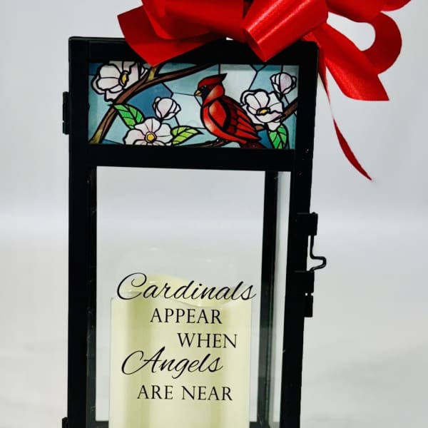 Black lantern with a red bow and a candle reading Cardinals appear when angels are near