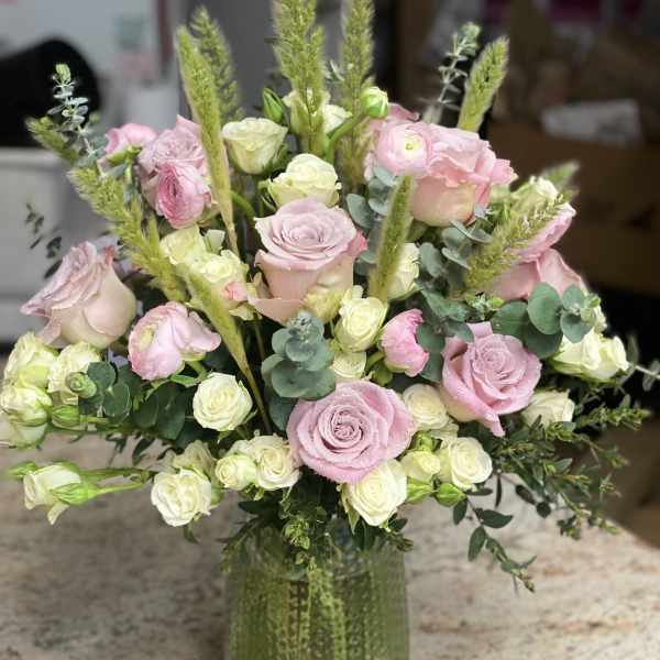 Pink and white roses arranged in a green glass vase