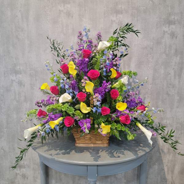 Large mixed bouquet in a wicker basket with pink roses, yellow callas, and purple flowers