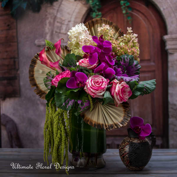Pink and purple floral arrangement in a dark vase with decorative fans
