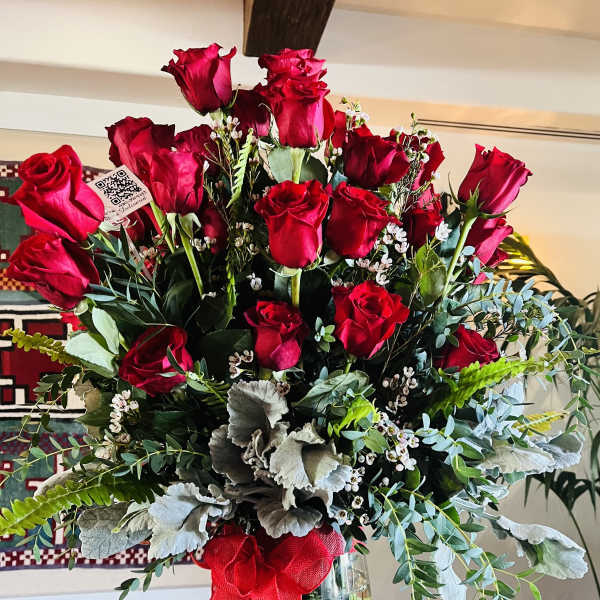 Red roses arranged in a clear glass vase with greenery and a red ribbon