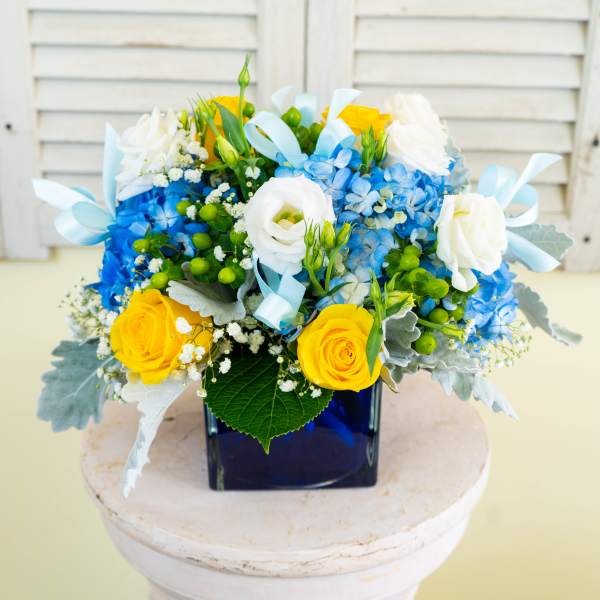 Blue and yellow floral arrangement in a square vase