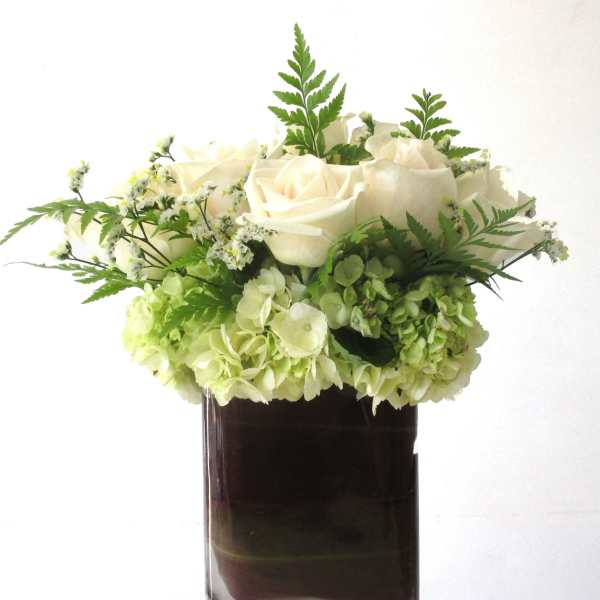 Low arrangement of white roses and green hydrangeas in a dark glass vase