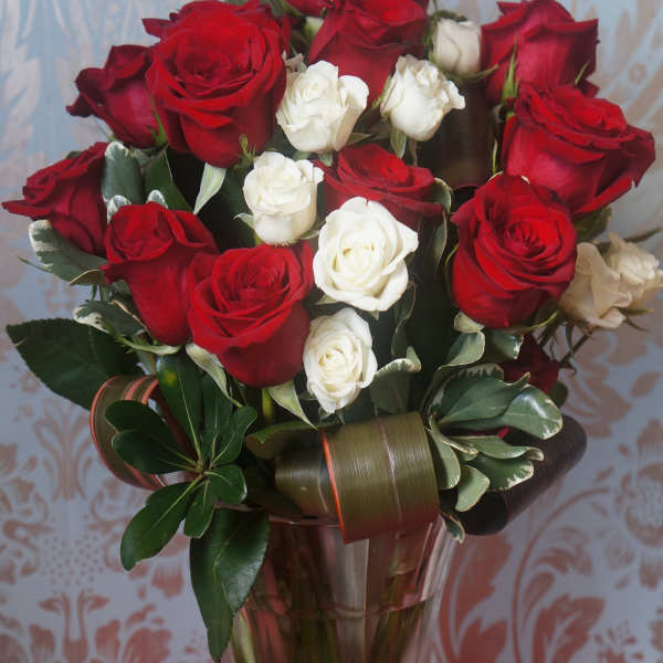 Tall clear vase of red and white roses with decorative looped green leaves