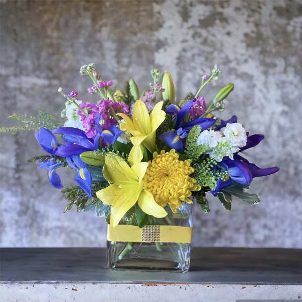 Bouquet of yellow lilies, blue irises, and white blooms in a glass vase