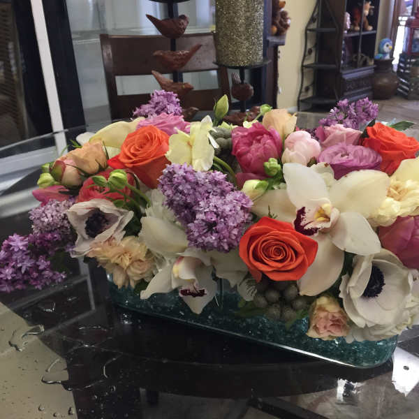 Mixed bouquet of roses, orchids, and lilac in a glass vase