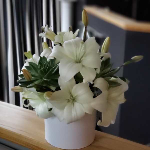 White lilies arranged in a white cylindrical vase