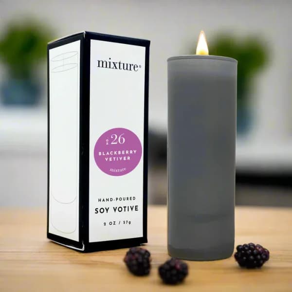 Gray soy votive candle beside its box with blackberries on a table