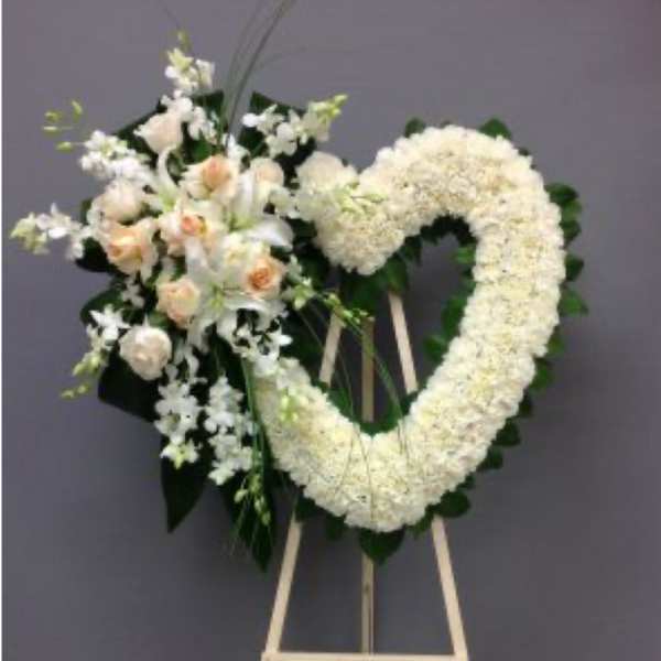 Heart-shaped white floral wreath on an easel with a small bouquet of pale roses
