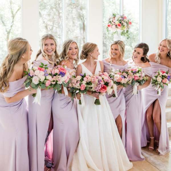 Bridesmaids and bride holding pastel flower bouquets indoors