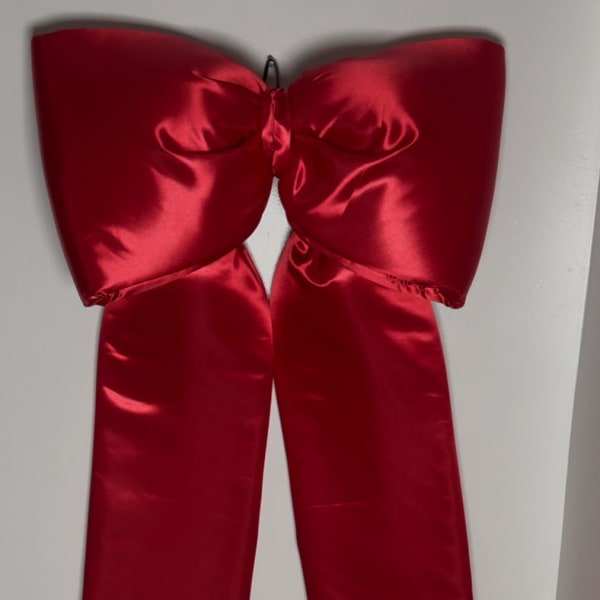 Large red satin bow with long ribbon tails hanging on a wall