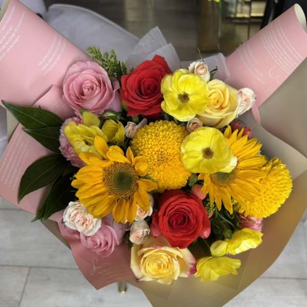 Mixed bouquet of roses, sunflowers, and yellow blooms wrapped in pink paper