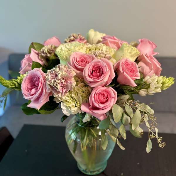 Pink roses and pale flowers arranged in a glass vase