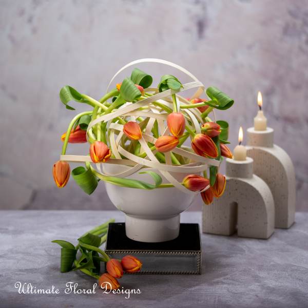 Orange tulips arranged in a white vase with looping ribbon accents