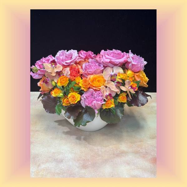 Pink and orange roses arranged in a white bowl vase