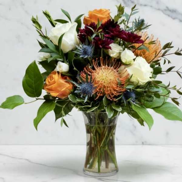 Bouquet of orange, white, and burgundy flowers in a clear glass vase