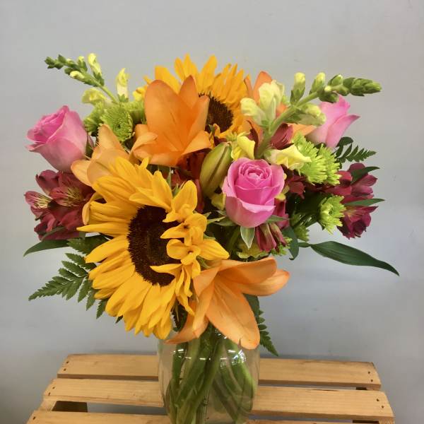 Mixed bouquet of sunflowers, pink roses, and orange lilies in a glass vase