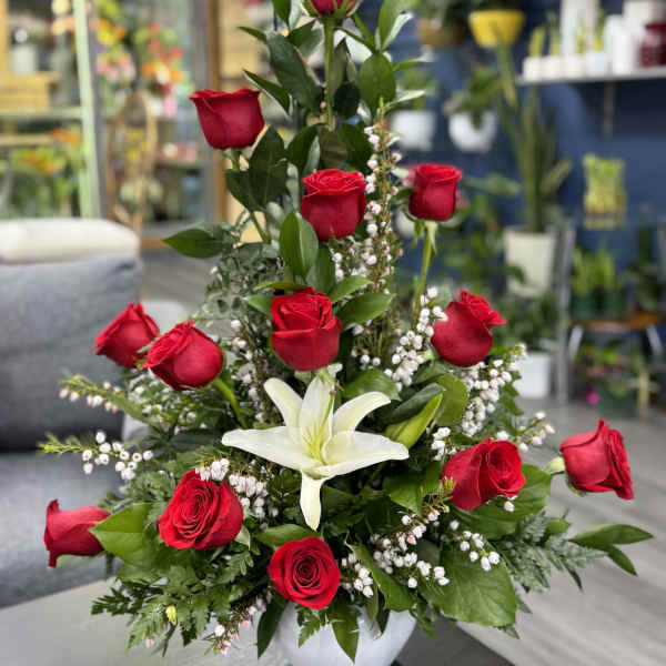 Tall arrangement of red roses and a white lily in a white vase