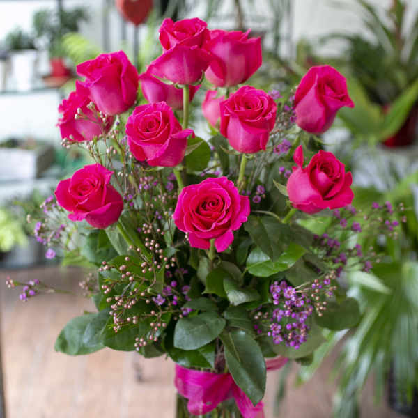 Pink roses arranged in a clear glass vase with small purple filler flowers.