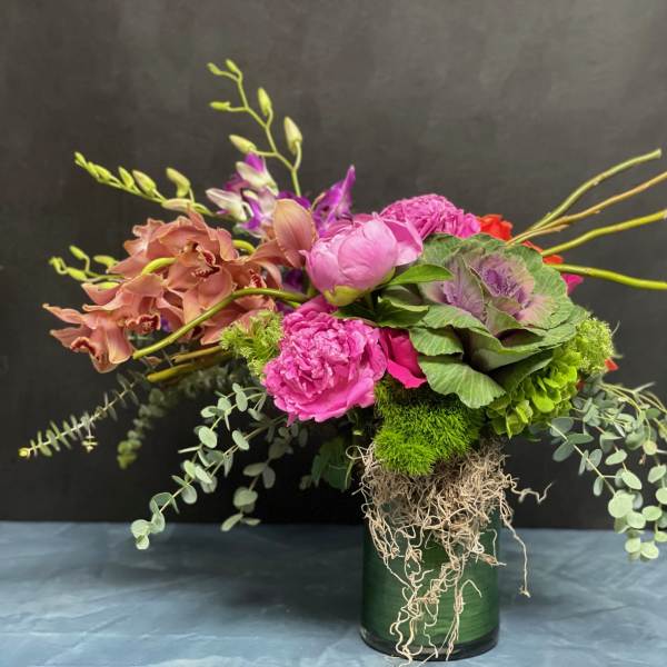 Asymmetrical arrangement with pink peonies, peach orchids, and green accents in a glass cylinder vase