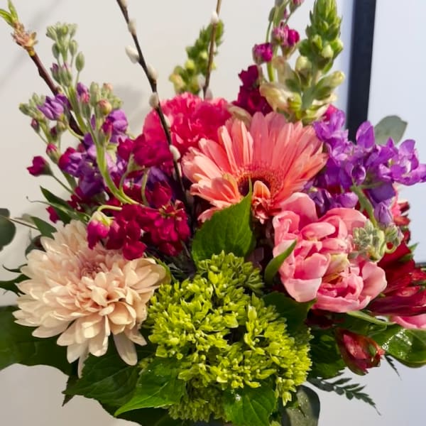 Mixed bouquet of pink, purple, and cream flowers in a glass vase