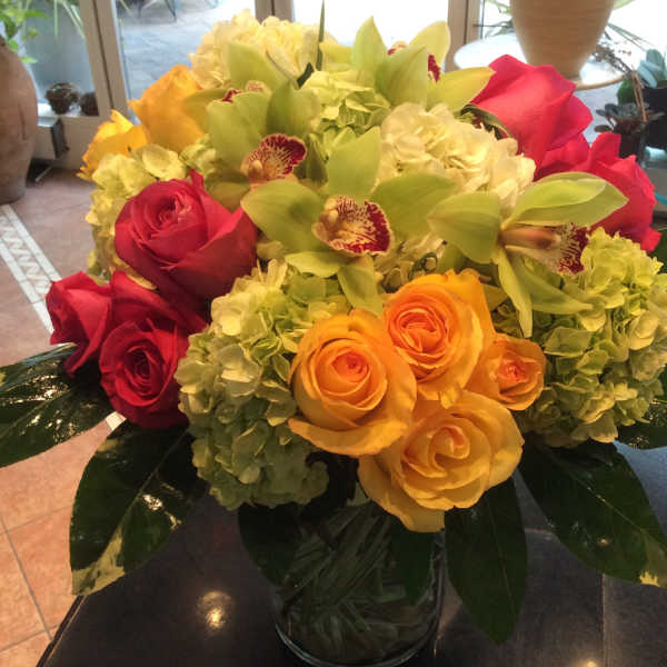Bouquet of red and yellow roses with green orchids in a glass vase