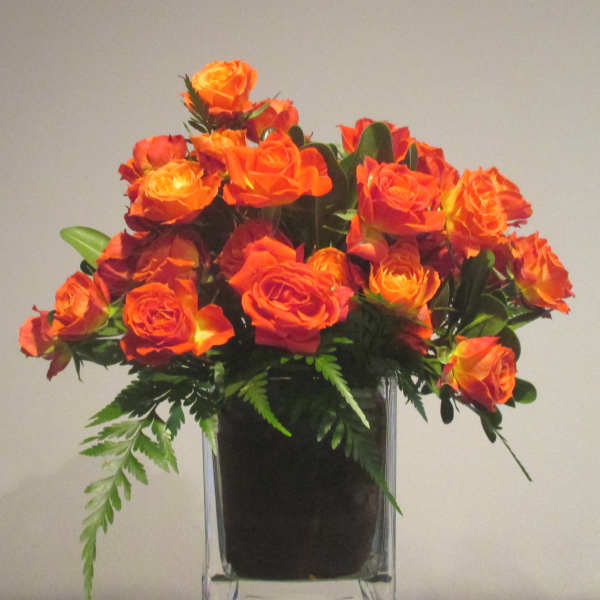 Orange and yellow spray roses arranged in a clear glass cube vase
