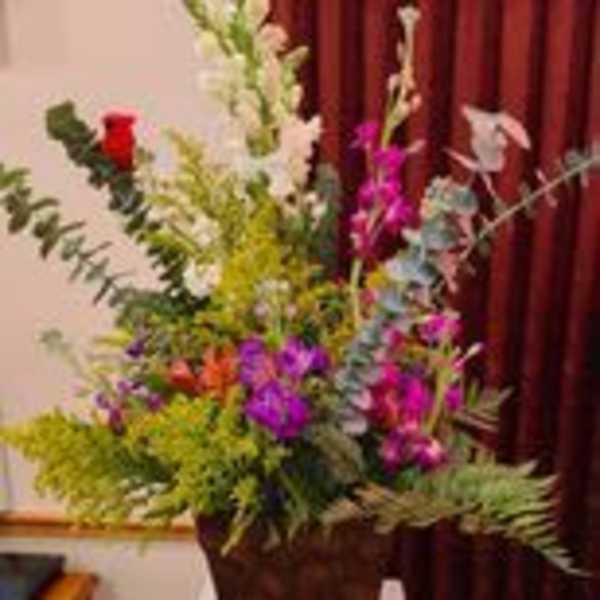 Tall mixed floral arrangement in a dark urn on a table