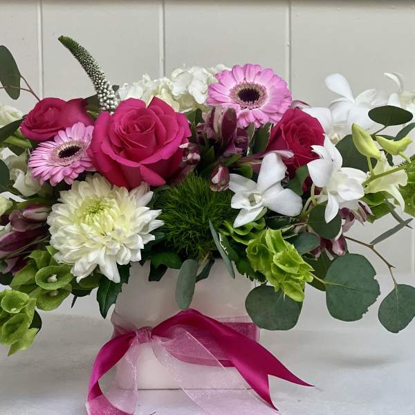 Pink and white mixed flower arrangement in a white vase with a pink ribbon