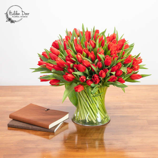 Red tulip bouquet in a clear glass vase on a wooden table