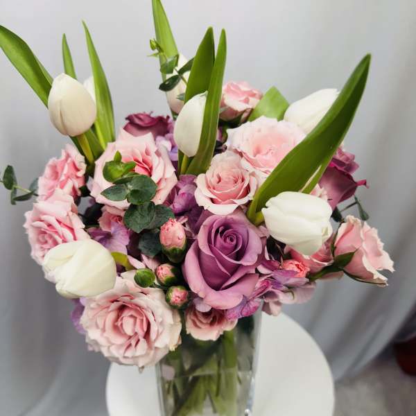 Pink and purple roses with white tulips in a clear glass vase