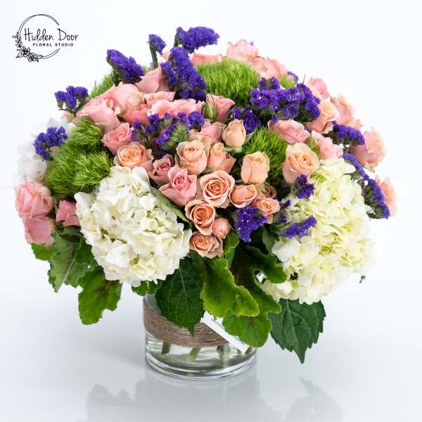 Pink roses, white hydrangeas, and purple filler flowers in a glass vase