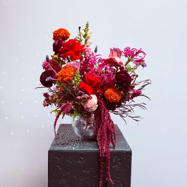 Bright mixed bouquet in a mirrored vase with red, pink, and orange blooms
