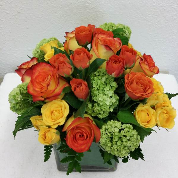 Bouquet of orange and yellow roses with green hydrangeas in a square glass vase