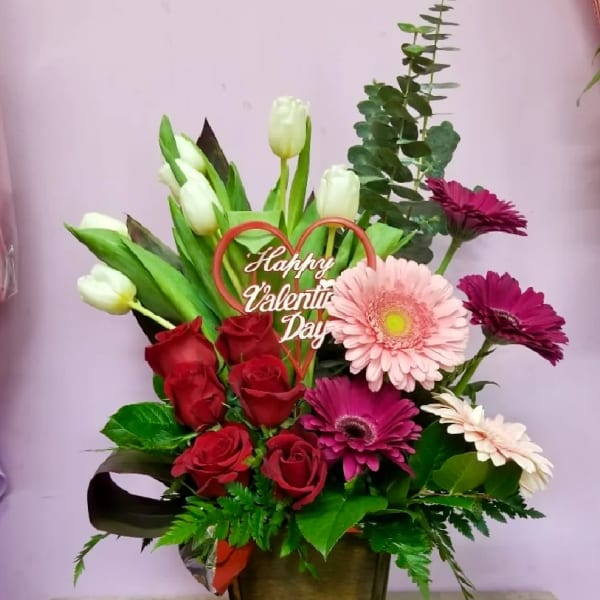 Mixed bouquet with roses, tulips, and gerbera daisies in a wooden container