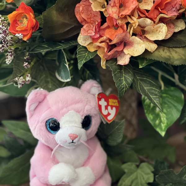 Pink plush cat beside an orange floral arrangement