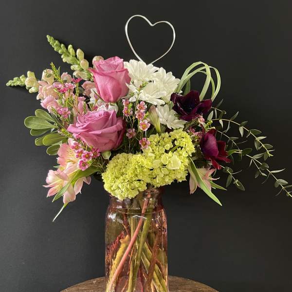 Mixed bouquet of pink roses, white daisies, and dark orchids in a glass vase