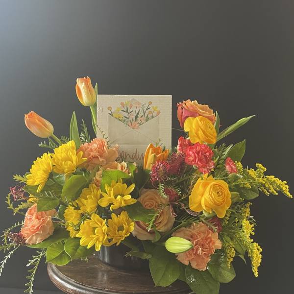 Mixed bouquet in a low container with yellow, orange, and pink flowers