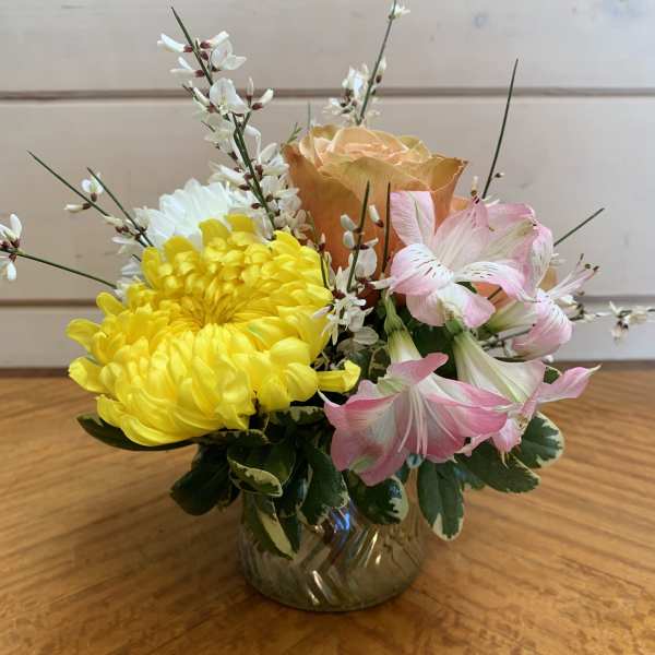 Yellow and pink flowers arranged in a small glass vase