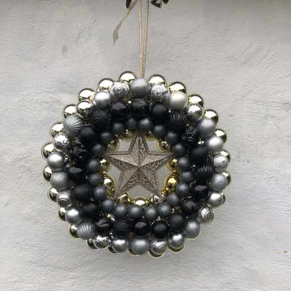 A circular ornament wreath with black, silver, and gold baubles and a star center