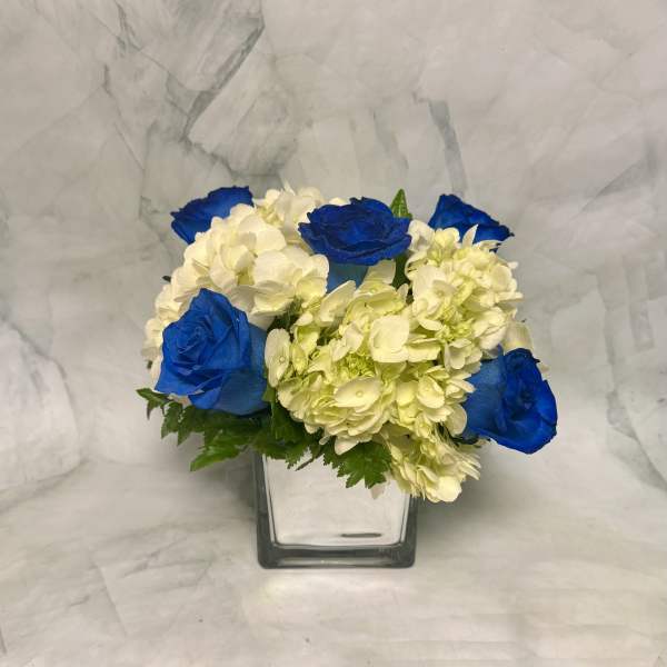 Blue roses and white hydrangeas in a square glass vase